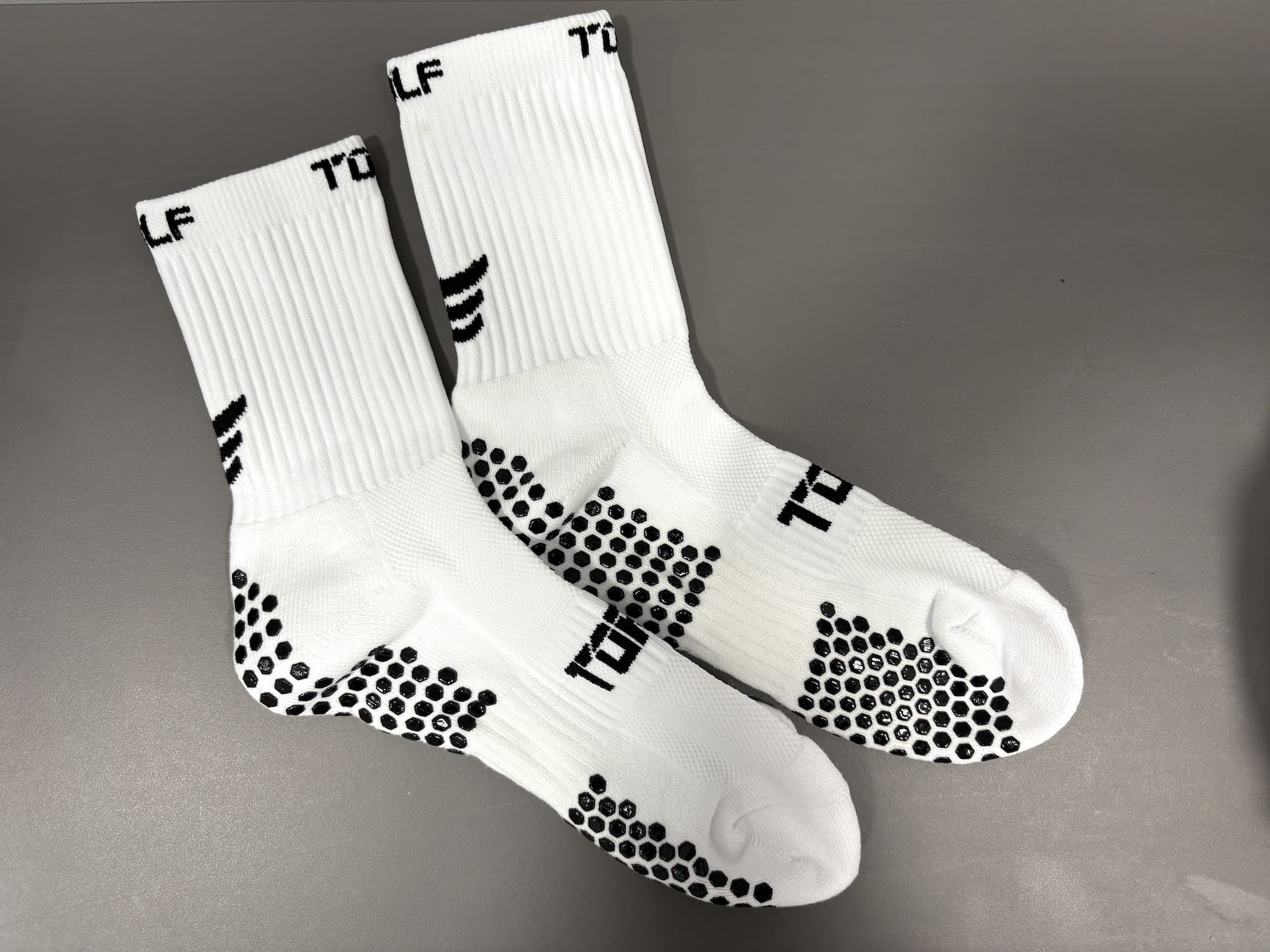 Pair of white Torn golf socks with grey spots on a grey background.